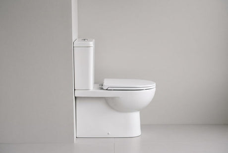 White close-coupled toilet with square cistern photographed from the side against grey wall