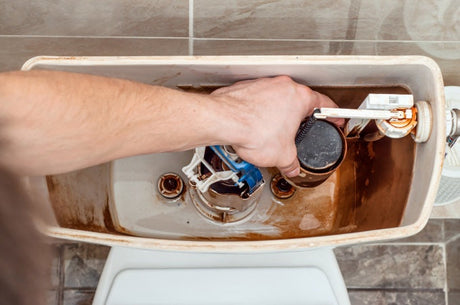 Hand replacing toilet tank flush valve and internal components with visible mineral buildup.