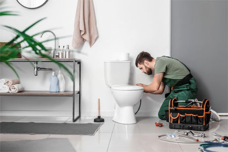 Plumber repairing a toilet in a modern bathroom with tools and supplies