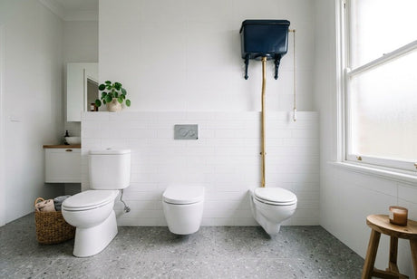 Three toilet cistern types side by side in white tiled bathroom