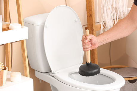 hand using plunger to unclog toilet in bathroom with open lid