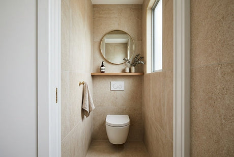 Narrow powder room with travertine tiles, wall-hung toilet, timber shelf and round gold mirror
