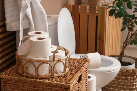 White toilet beside wicker basket holding toilet paper rolls in styled bathroom