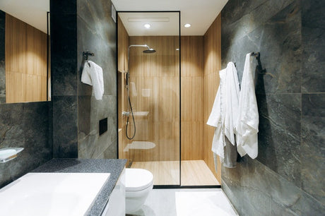 Modern bathroom with wood tile shower, dark stone walls, white towels, and vanity.