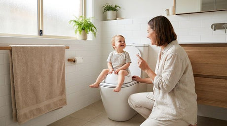 Smiling toddler sitting on toilet trainer seat with mother kneeling beside