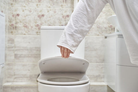 Woman closing the lid of a modern white toilet in a bright contemporary bathroom
