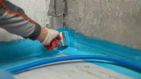 Construction worker applying waterproofing membrane with a brush in the corner of a bathroom during renovation