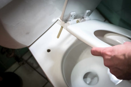 Close-up of hands installing or removing a white toilet seat lid from a toilet bowl