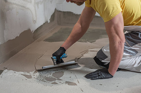 Worker using a trowel to apply liquid waterproofing membrane on a bathroom floor