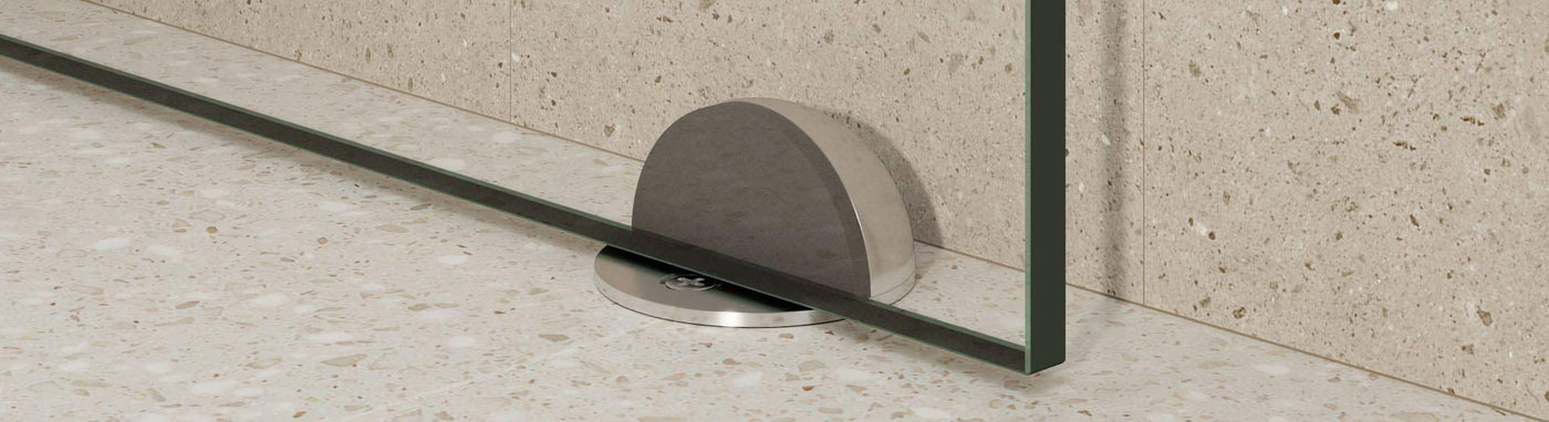 Brushed half-dome floor door stop securing a glass shower screen on terrazzo tiles.