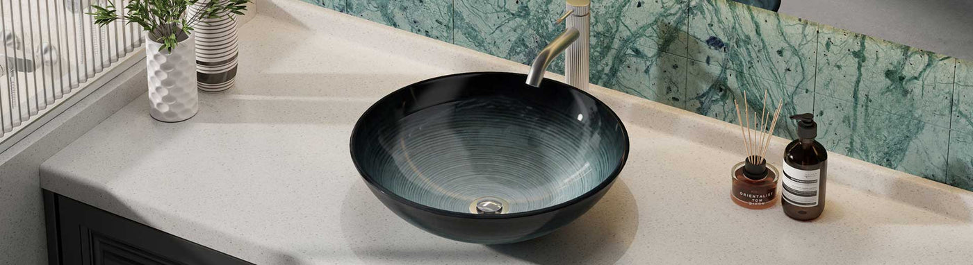 Round black and blue glass basin on a white vanity top with green marble splashback and modern accessories.