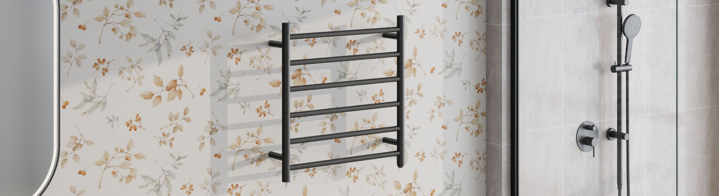 Ladder-style heated towel rail in matte black mounted near a shower on light stone tiles.