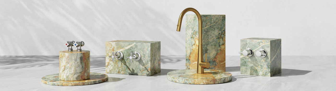 Polished brass and chrome laundry tapware displayed on green-toned marble stands.