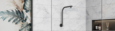 Curved matte-black wall shower arm over large white marble tiles, with a tropical leaf mural at the edge.