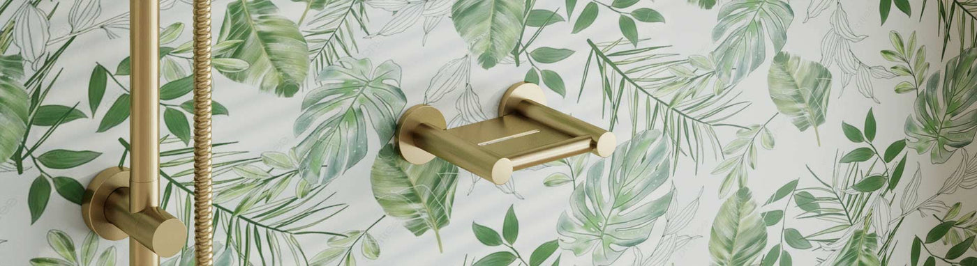 Brushed-gold wall-mounted soap dish set near a matching shower rail on a leafy patterned wall.