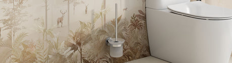 Wall-mounted stainless toilet brush with a frosted cup beside a modern white toilet against a soft botanical wall.