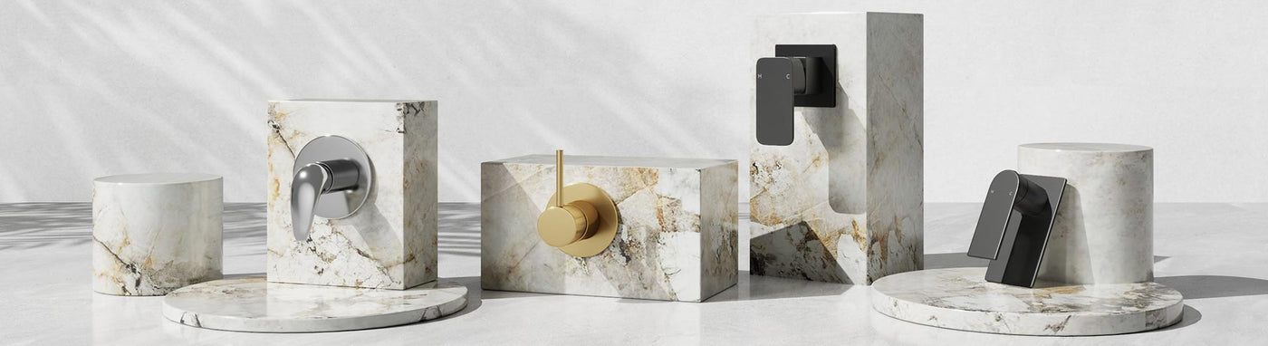 Single-outlet wall mixer taps in chrome, brushed gold and matte black on marble plinths.